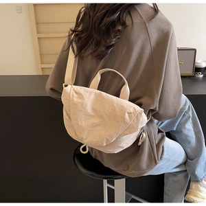 Minimalist cream nylon crossbody dumpling bag shown in a stylish lifestyle cafe setting