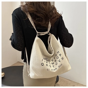 Detailed back view of a beige canvas hobo backpack with black letter print on a model