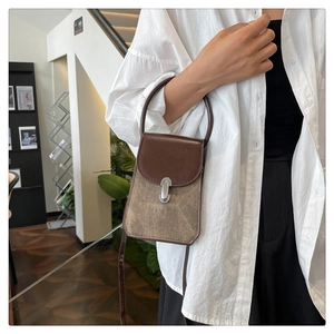 French style crossbody bag with leather stitching and metal lock worn in a cozy room