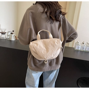 Beige pleated fabric crossbody bag shown on model in a cafe setting with shoulder strap