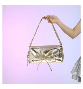 Detail of a metallic gold PU handbag featuring a delicate bow and woven leather strap