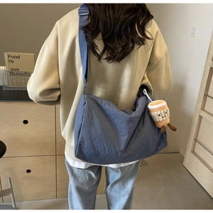 Rear view of a model wearing a large blue nylon crossbody bag with a cute plush pendant