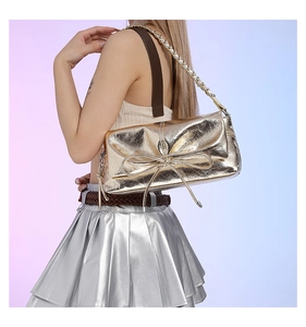 Golden bow handbag with crinkled texture and metal chain strap worn by a model