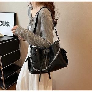 Detailed macro view of black PU leather shoulder bag featuring silver chains and side pockets