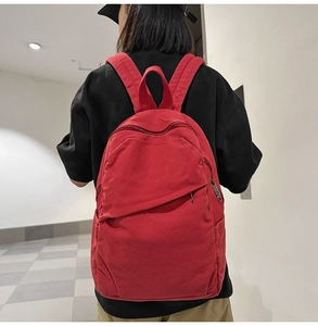 Rear view of a large red canvas backpack worn by a model in a minimalist room