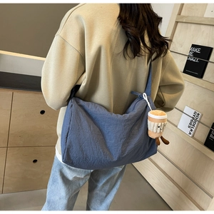 Close-up of large blue crossbody bag with plush coffee cup charm and wide strap