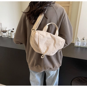 Fashionable pleated fabric crossbody bag in cream white worn by a model in a cafe