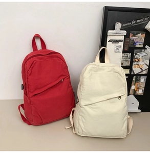 Detail of red and off-white canvas backpacks featuring a diagonal zipper pocket and side label
