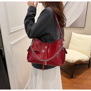 Detail view of a large red glossy PU leather shoulder bag with silver chain and strap