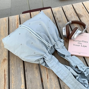 Detail of light blue nylon tote bag with silver studs on a wooden bench outdoors