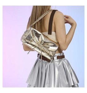 Detail of metallic gold bow shoulder bag with silver chain strap on silver dress