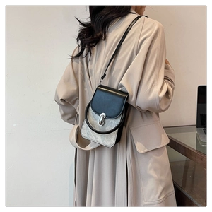 Side view of modern black and silver crossbody bag worn over a beige trench coat