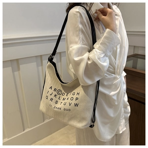 Detail of minimalist cream canvas tote bag with black strap and letter print on model