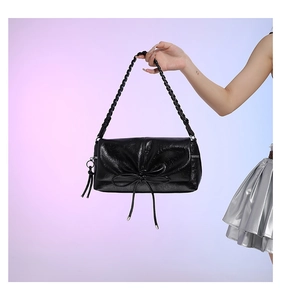 Detail of black glossy PU leather handbag featuring woven handle and bow decoration