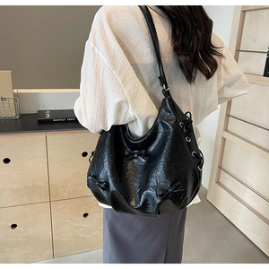 Detail of black pleated PU leather crossbody bag featuring bow accents on a female model
