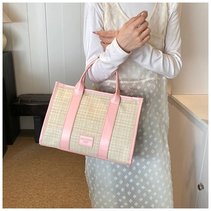 Detailed shot of straw tote with pink faux leather trim and branding label on the side