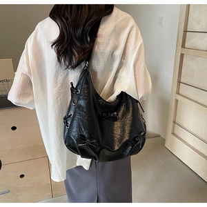 Detail of black PU leather tote bag with bow accents and metal eyelets on model's shoulder