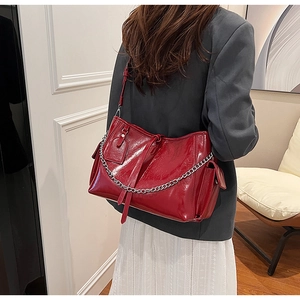 Detail view of red glossy patent leather shoulder bag with silver chain and side ribbon