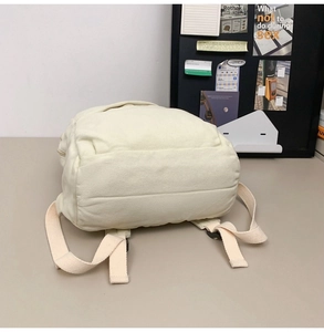 Detail view of the cream-colored canvas backpack showing padded straps and durable fabric texture