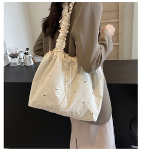 Detail of cream tote bag featuring ruffled shoulder straps and rivet embellishments