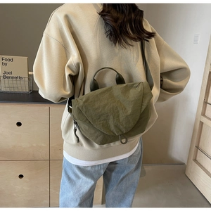 Olive green nylon crossbody bag with pleated texture shown on a model in a home setting