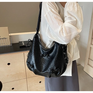 Detail of black pleated faux leather tote bag featuring a decorative bow and side metal eyelets