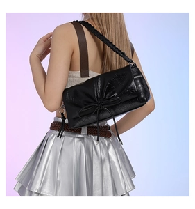Rear view of model wearing a black PU leather shoulder bag with a stylish bow and woven strap