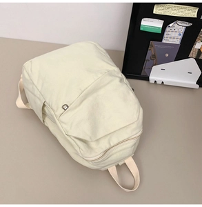 Detailed 45-degree angle view of the cream white canvas backpack with front zipper pocket