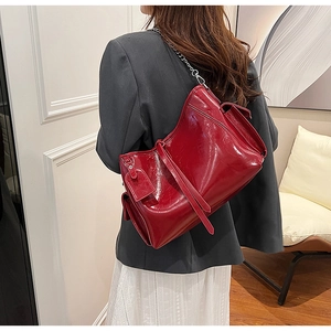 Detail view of a red shiny PU leather crossbody bag with chain strap on a model