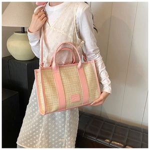 Detail of straw woven tote bag featuring pink faux leather trim and brand label