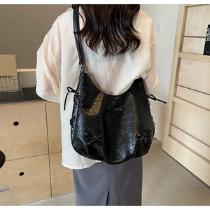 Detail view of black PU leather shoulder bag with decorative bows and drawstring eyelets