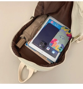 Interior storage space of cream canvas backpack with tablet, umbrella, and essentials