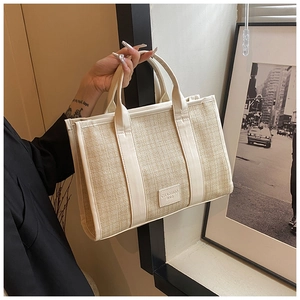 Detail of woven straw texture and leather brand patch on minimalist cream tote bag