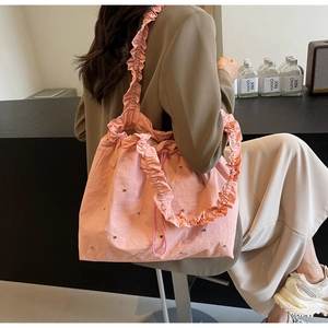 Pink fabric tote bag with ruffled shoulder strap and silver ornaments shown in interior