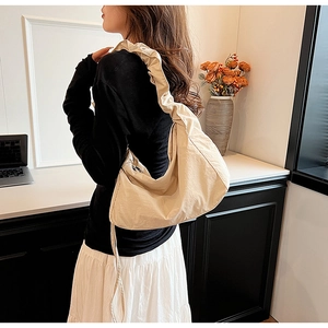 Detail of a beige nylon crossbody bag with unique pleated shoulder strap on a model