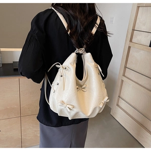 Detail of off-white PU leather backpack with bow knots and drawstring on model's back