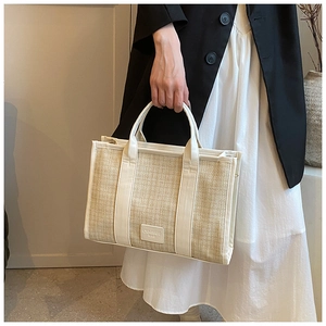 Detail of straw woven tote bag with white leather trim and hand-held handle strap