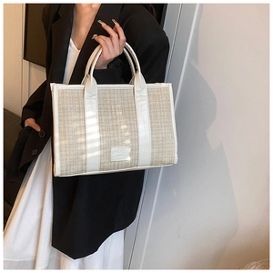Detail view of woven straw tote bag with white leather straps and textured material