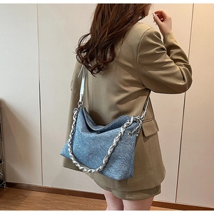 Detail of blue denim textured shoulder bag with thick silver metal and leather chain strap