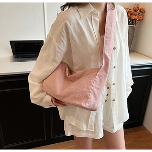 Close-up of pink nylon crossbody bag with wide shoulder strap worn by a model in interior