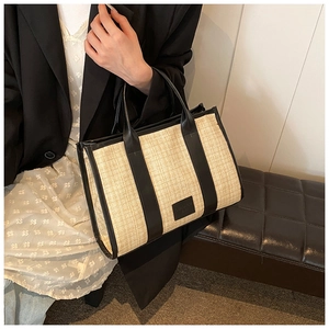 Detailed view of beige woven straw tote bag with black leather trim and top handles