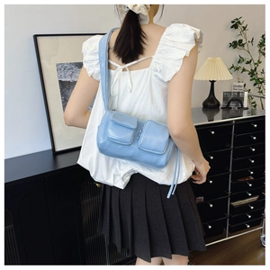 Detail view of a soft light blue glossy PU leather shoulder bag with double front pockets