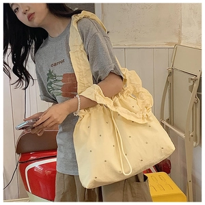 Detail of canvas tote bag with metal stud embellishments and ruffled drawstring shoulder strap