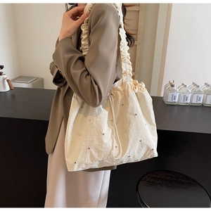Detail of cream drawstring tote bag featuring silver studs and ruffled shoulder strap