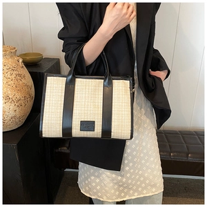 Detail of summer woven tote bag featuring black faux leather trim and brand logo patch
