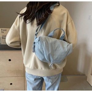 Close-up of light blue pleated crossbody bag with drawstring detail and fabric strap