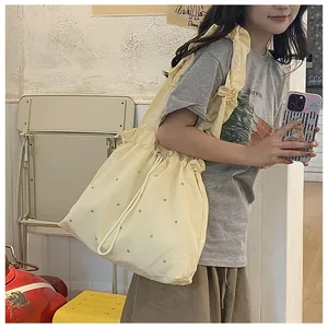 Close-up of beige canvas pleated tote bag with silver rivet studs and drawstring closure