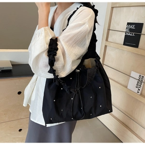 Detail view of black nylon tote bag featuring silver rivets and ruffled shoulder strap