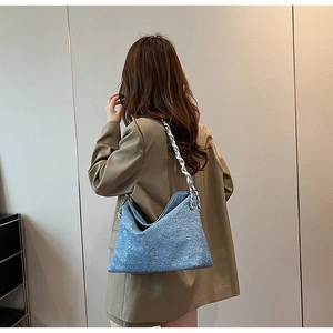 Detail of blue tweed shoulder bag featuring a metallic chain strap on a blazer model