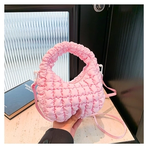 Pink puffy cloud crossbody bag with pleated texture and adjustable strap on black background
